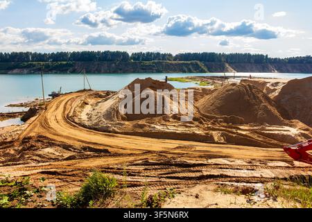 Carrière de sable inondée vaste avec d'énormes monticules dorés, des routes de terre sinueuses avec des traces de pneus et une eau turquoise cristalline Banque D'Images