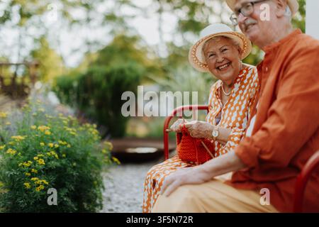 Heureux couple senior assis ensemble dans le banc de jardin, souriant et regardant la caméra. Banque D'Images