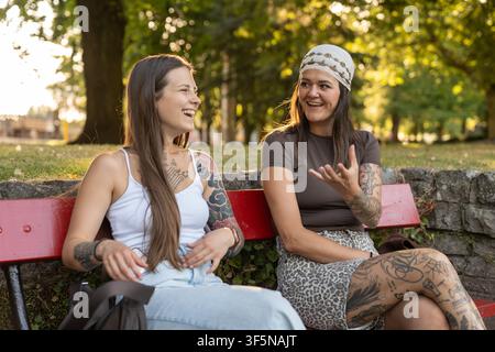 Jeunes femmes heureuses bavardant et riant sur un banc de parc Banque D'Images