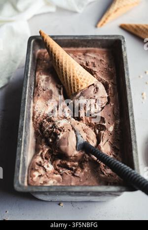 Scoopant de la glace au chocolat marbrée d'une poêle en métal Banque D'Images