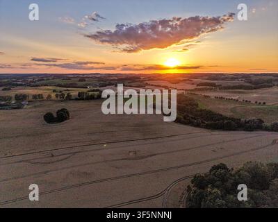 Coup d'œil aérien d'un coucher de soleil sur une campagne ondulée avec des nuages dramatiques du soir et des terres agricoles dorées Banque D'Images