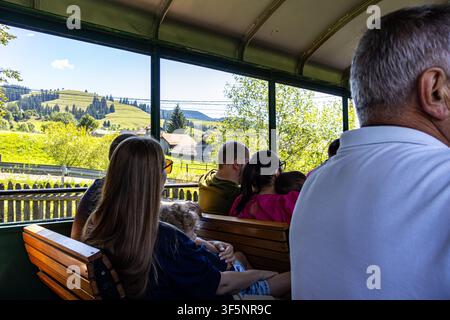 Une prise de vue horizontale intérieur-extérieur montrant des passagers assis à l'intérieur d'un wagon de train en bois ouvert sur les côtés, profitant d'une balade pittoresque à travers une montagne Banque D'Images