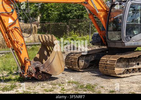 Un plan horizontal en gros plan détaillé mettant l'accent sur la benne en acier massive et les chenilles métalliques lourdes d'une pelleteuse industrielle orange. Banque D'Images