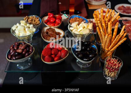 Une table de banquet élégante présente une variété d'apéritifs, notamment des bols de fraises fraîches, des olives noires, des bâtonnets de pain, des noix, des cubes de fromage, dr Banque D'Images