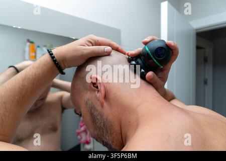 Homme se rasant la tête avec un rasoir électrique dans la salle de bain Banque D'Images