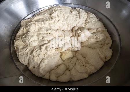 Pâte brute fraîche dans un grand bol mélangeur industriel en métal brillant, préparée pour la cuisson de délicieux produits de boulangerie dans une boulangerie professionnelle Banque D'Images