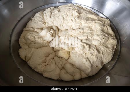 Pâte blanche fraîche levant dans un grand bol mélangeur industriel en acier inoxydable, prête pour la production de pain dans un environnement de cuisine professionnelle, brute Banque D'Images