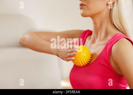 Une femme effectue un auto-massage à l'aide d'une balle de massage à pointes sur sa poitrine, favorisant le soulagement du stress et améliorant la santé des pieds grâce au relâchement myofascial te Banque D'Images