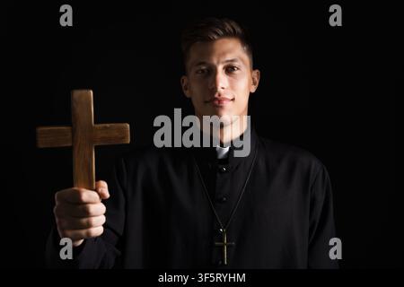 Portrait d'un prêtre avec une croix en bois sur fond noir Banque D'Images