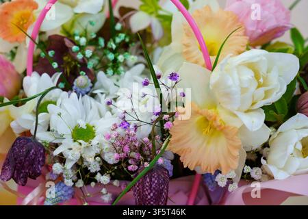 Un panier contient différents types de fleurs, notamment des marguerites, des lys et des roses. L'arrangement présente des couleurs vives et diverses formes. Banque D'Images