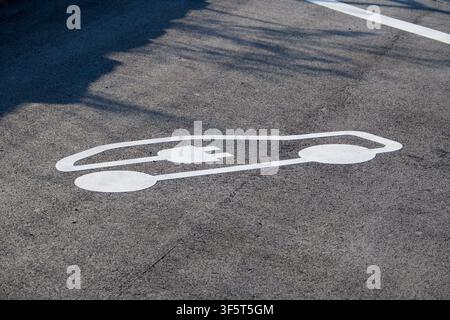 Symbole de recharge d’un véhicule électrique blanc peint sur de l’asphalte sombre dans une place de parking réservée aux VE, représentant le transport durable et la mobilité verte Banque D'Images
