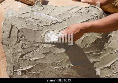 Maçon appliquant un plâtre de ciment frais avec une truelle sur un mur extérieur, détail de rénovation. Banque D'Images
