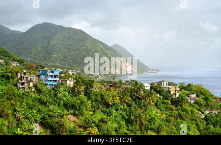 Vue panoramique d'un village côtier avec des maisons colorées, des collines tropicales luxuriantes et les eaux bleues de la mer des Caraïbes à Dominique Banque D'Images