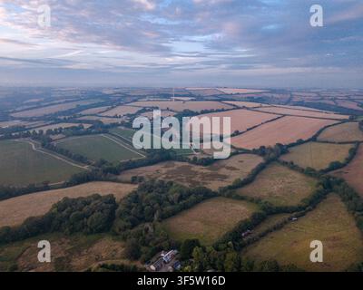 Vue aérienne du paysage rural du Cornwall, en Angleterre, pendant l'heure dorée avec de la brume se formant à l'arrière-plan sur des champs en mosaïque et des pâturages verts Banque D'Images