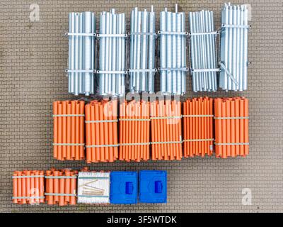 Vue aérienne de faisceaux de tuyaux en métal argenté et de tuyaux en plastique orange disposés sur un chantier de construction pavé en Pologne. Banque D'Images