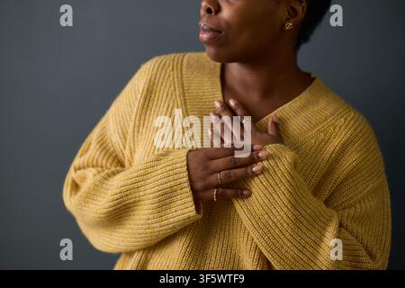 Jeune femme afro-américaine tenant les mains sur le cœur, exprimant la gratitude et les soins personnels. L'image représente le bien-être mental, la pleine conscience et le marketing de la santé émotionnelle Banque D'Images