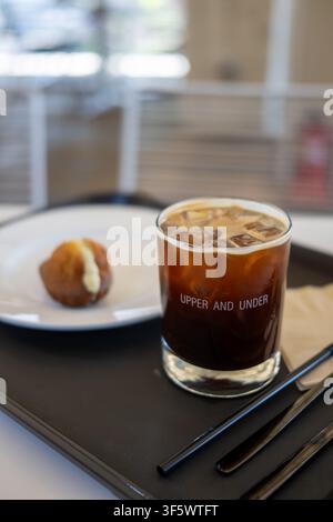 Un café glacé dans un verre de marque et une madeleine fourrée sur un plateau dans un café à Gangnam, Séoul. Banque D'Images