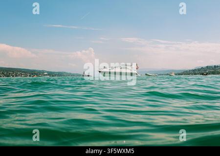 Zurich, Suisse, 2 août 2026. Vue basse de la surface de l'eau d'un yacht de luxe flottant sur le lac de Zurich sous un ciel d'été lumineux avec un mou éloigné Banque D'Images