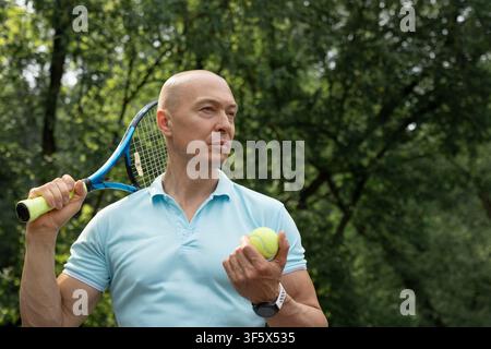 Portrait d'un joueur de tennis caucasien confiant tenant une raquette et une balle de tennis avant un match en plein air. Concept de mode de vie sain et actif et de sport amateur. Banque D'Images