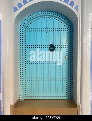 Porte voûtée turquoise élégante avec clous décoratifs et heurtoir noir, typique de l'architecture marocaine à Chefchaouen dans la Cité Bleue. Banque D'Images