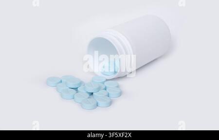 Comprimés bleus s'échappant d'une bouteille de médicaments blanche ouverte sur un fond clair et net Banque D'Images