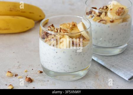 Deux verres de pudding aux graines de chia avec des tranches de banane et des noix sur fond pastel Banque D'Images