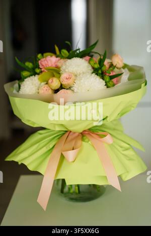 Bouquet élégant de chrysanthèmes blancs et de petites roses roses enveloppé dans du papier vert clair avec un ruban rose doux, parfait pour les célébrations Banque D'Images