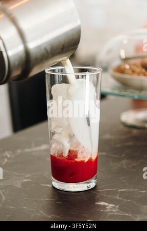 Du lait froid est versé sur de la glace et de la purée de fraises pour créer la couche centrale d’une boisson glacée colorée. Boisson rafraîchissante de café préparée à la main. Banque D'Images