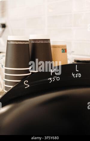 Gobelets à emporter empilés disposés derrière le comptoir du café, prêts à servir des boissons chaudes. Essentiels de café dans un intérieur moderne. Banque D'Images
