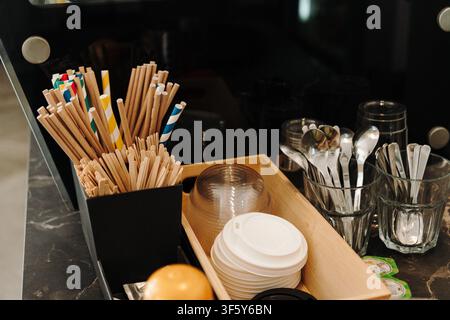 Comptoir de café avec pailles en papier, mélangeurs en bois, couvercles jetables, cuillères et accessoires de service. Poste de travail organisé dans un café moderne Banque D'Images