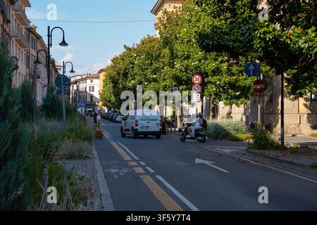 Bergamo, Italie – 16 juin 2026 : Photo dynamique du trafic urbain montrant une camionnette de livraison et un scooter roulant dans une rue de ville italienne bordée de végétation luxuriante Banque D'Images