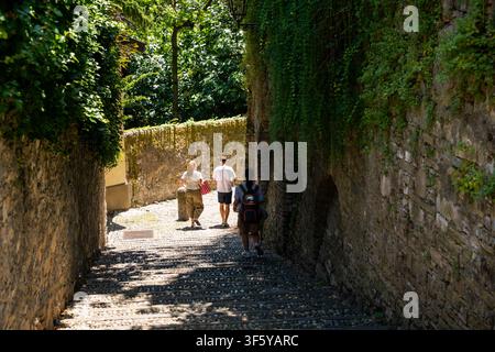 Bergamo, Italie – 17 juin 2026 : Vue en hauteur sur des voyageurs descendant une escalier pavé ensoleillé encadré par des murs de pierre historiques recouverts de verdure Banque D'Images