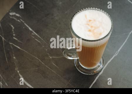 Vue aérienne d'un latte fraîchement préparé avec une mousse de lait crémeuse dans une tasse en verre. Composition minimaliste propre de café avec espace pour du texte. Banque D'Images
