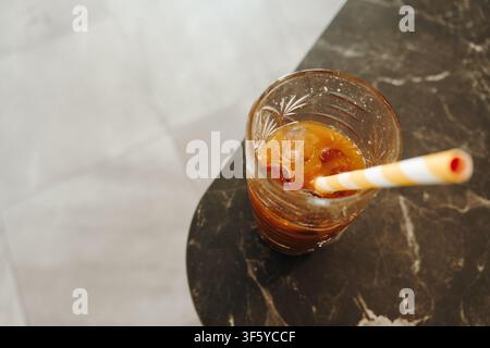 Vue de dessus d'un verre de café glacé avec des glaçons et une paille en papier rayée. Boisson froide rafraîchissante servie sur une table en marbre d'un café. Banque D'Images