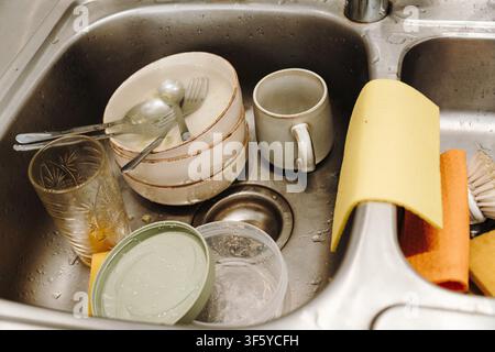 Plats, verres et couverts usagés empilés dans un évier de cuisine avant le lavage. Routine de nettoyage quotidienne dans une cuisine de café ou de restaurant. Banque D'Images