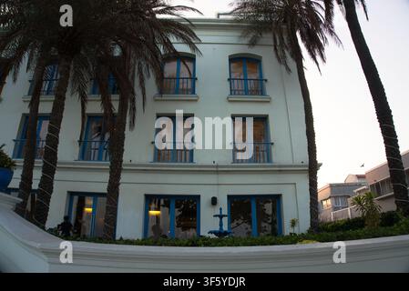 Bâtiment côtier blanc avec des fenêtres bleues à volets distinctives et de grands palmiers se dressant le long de la façade extérieure au crépuscule à Pondichéry Banque D'Images