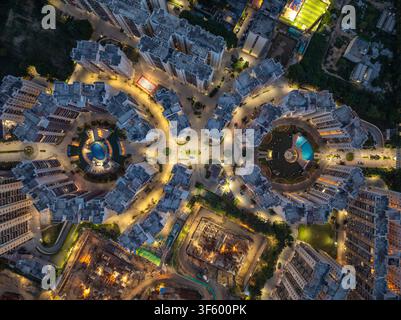 Vue aérienne d'un complexe résidentiel moderne la nuit mettant en vedette des immeubles d'appartements illuminés, des piscines circulaires et les travaux de construction environnants Banque D'Images