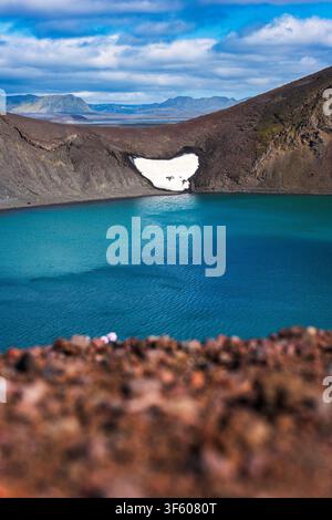 Vue aérienne à couper le souffle d'un lac glaciaire turquoise niché dans un cratère volcanique avec une parcelle de neige immaculée, des champs de lave sombres et lointains Banque D'Images