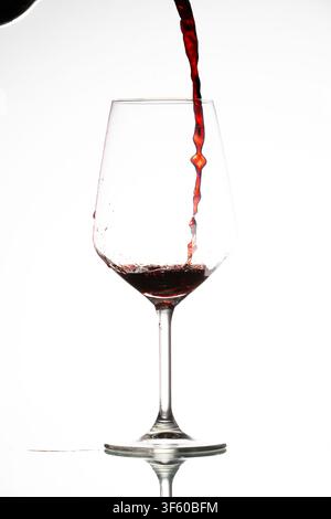Du vin rouge versé dans un verre transparent, créant des éclaboussures sur un fond blanc Banque D'Images