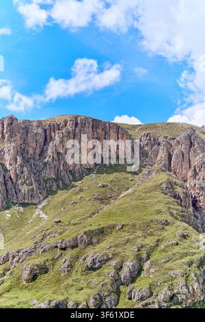 Crête rocheuse alpine rocheuse avec des pentes herbeuses vertes sous un ciel bleu parsemé de nuages blancs. Banque D'Images