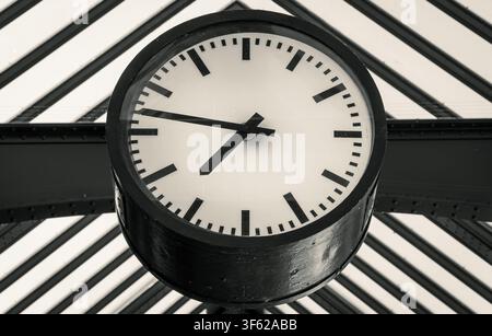 Close-up d'une horloge traditionnelle de gare montée sous une structure de toit historique en acier et verre à Berlin, Allemagne. Banque D'Images