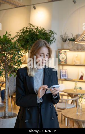 Femme d'affaires positive qui a réussi le directeur de restaurant envoyant des SMS sur son smartphone pendant la pause de travail. Banque D'Images