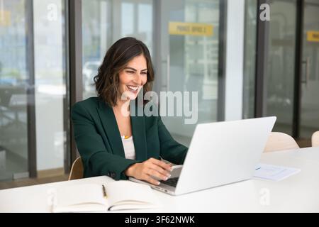 Femme d'affaires joyeuse ayant un appel vidéo sur son ordinateur portable Banque D'Images
