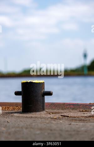 Boulon d'amarrage patiné sur un quai en béton à côté d'un calme port industriel Banque D'Images