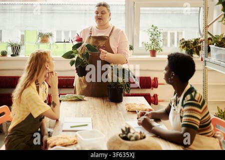 Jeunes femmes diverses assistant à un atelier de jardinage avec une instructrice caucasienne tenant une plante en pot. Image adaptée au marketing des petites entreprises et aux campagnes d'éducation communautaire Banque D'Images