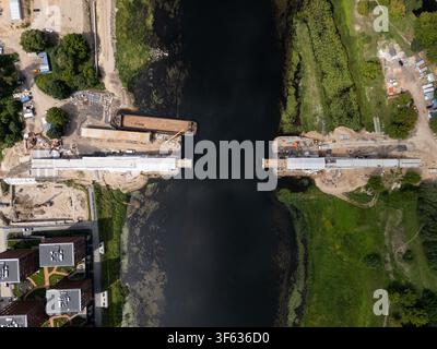 Vue aérienne d'un pont en construction au-dessus de la rivière avec des péniches et des engins de chantier visibles à Kaunas, comté de Kaunas, Lituanie. Banque D'Images