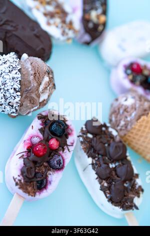 Ronde colorée de bâtonnets glacés maison au yaourt et au lait. Vanille et chocolat décorés de noix et de baies surgelées sur un fond bleu vif. Parfait pour une fête d'anniversaire d'enfants en été. Banque D'Images