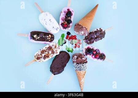 Ronde colorée de bâtonnets glacés maison au yaourt et au lait. Vanille et chocolat décorés de noix et de baies surgelées sur un fond bleu vif. Parfait pour une fête d'anniversaire d'enfants en été. Banque D'Images