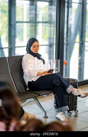 Femme musulmane voyageant à l'aéroport en utilisant un smartphone Banque D'Images
