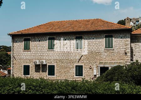 Maison en pierre traditionnelle avec volets verts et toit en tuiles sous un ciel bleu éclatant. L'architecture méditerranéenne classique reflète l'intemporalité Banque D'Images